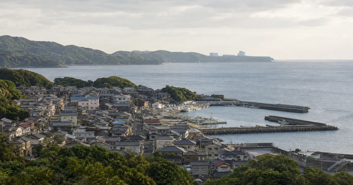 海辺の町と、遠景に小規模な産業設備の気配がある地域の関係を表した概念イメージ
