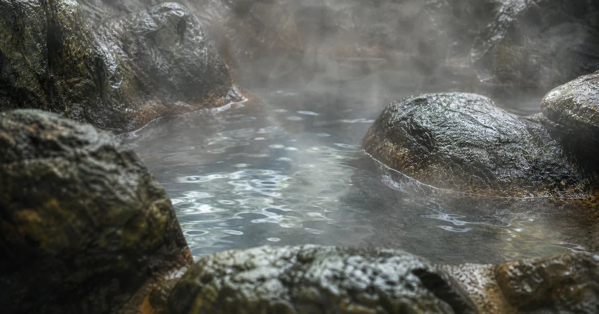 湯面と濡れた自然石、立ち上る湯気を接写した、つぼ湯を想起させるイメージ